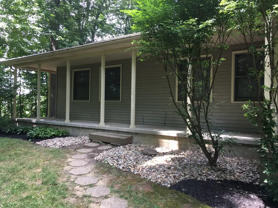 Covered Hidden Pines townhome porch with white columns, mature trees and landscaped stone beds